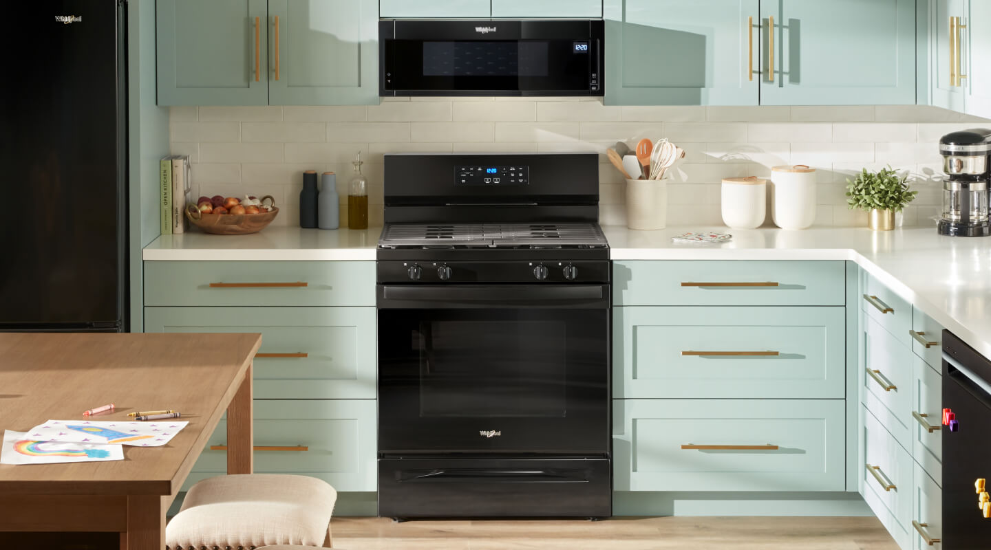 Black gas stove installed in a modern kitchen with teal cabinets and an over the range microwave installed above it