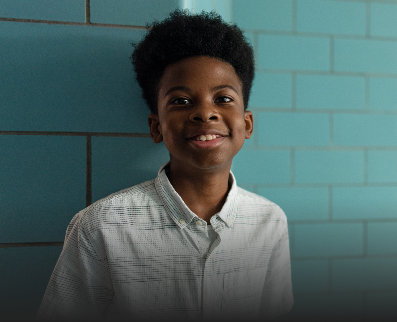 A smiling child stands against a blue-green wall