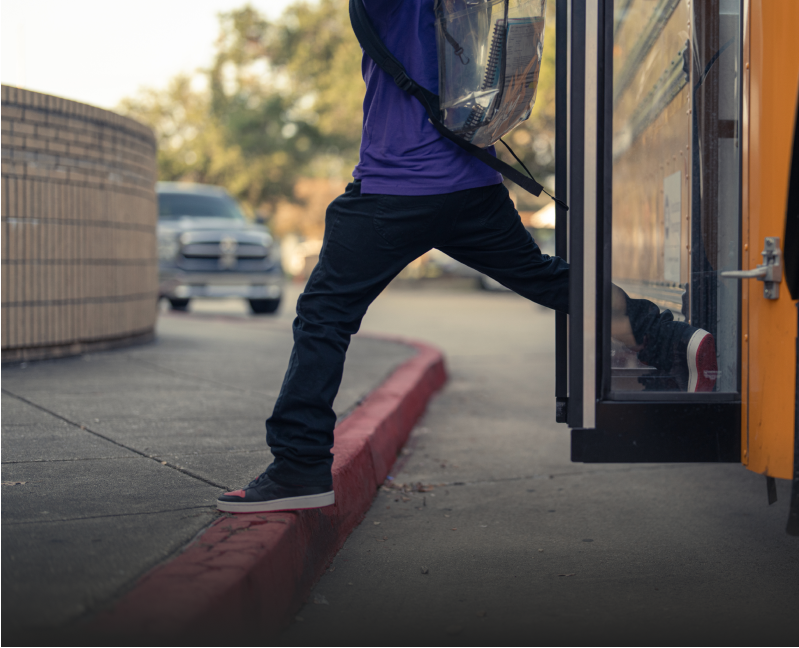 A child getting off a school bus onto the sidewalk curb