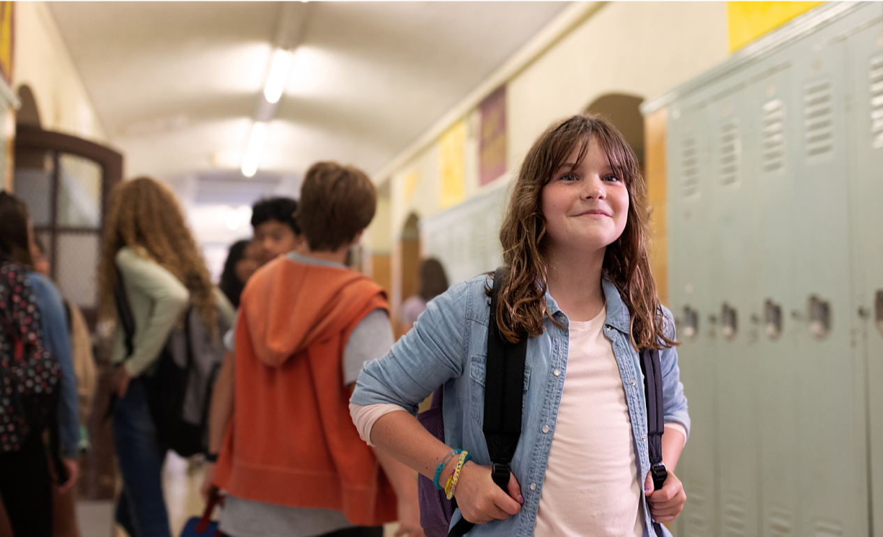 A smiling child in a school hallway with other kids behind them