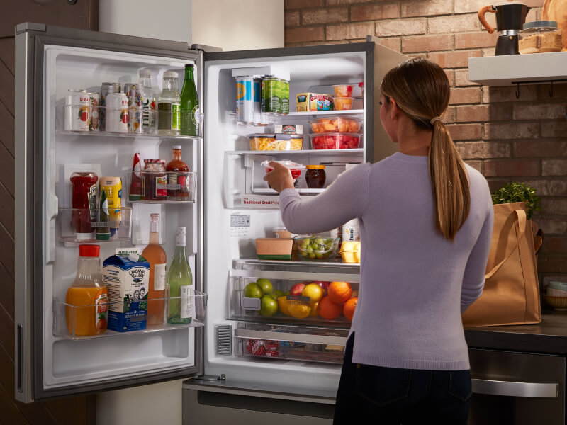 Woman loading food into a skinny refrigerator