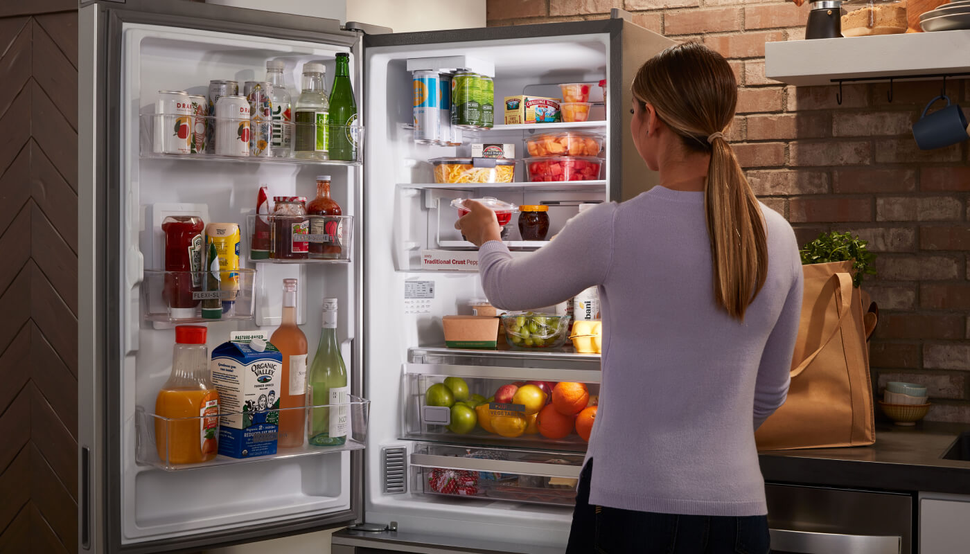 Woman loading food into a skinny refrigerator