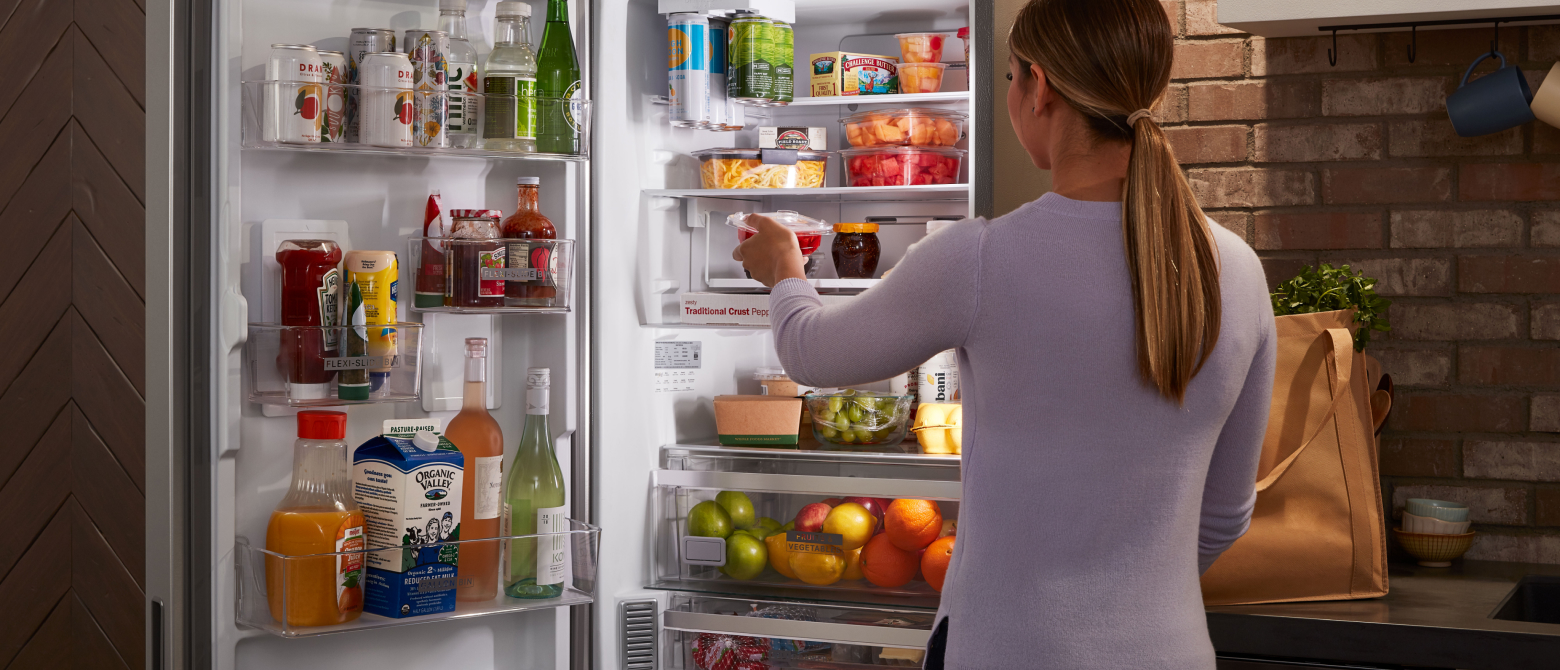 Woman loading food into a skinny refrigerator Woman loading food into a skinny refrigerator