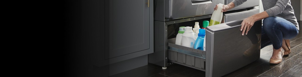 Person organizing cleaners inside a laundry machine pedestal