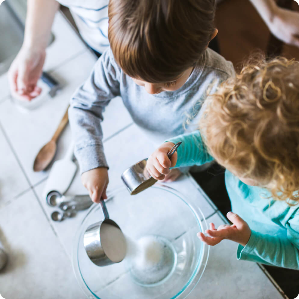 Young children pouring baking ingredients into a glass bowl