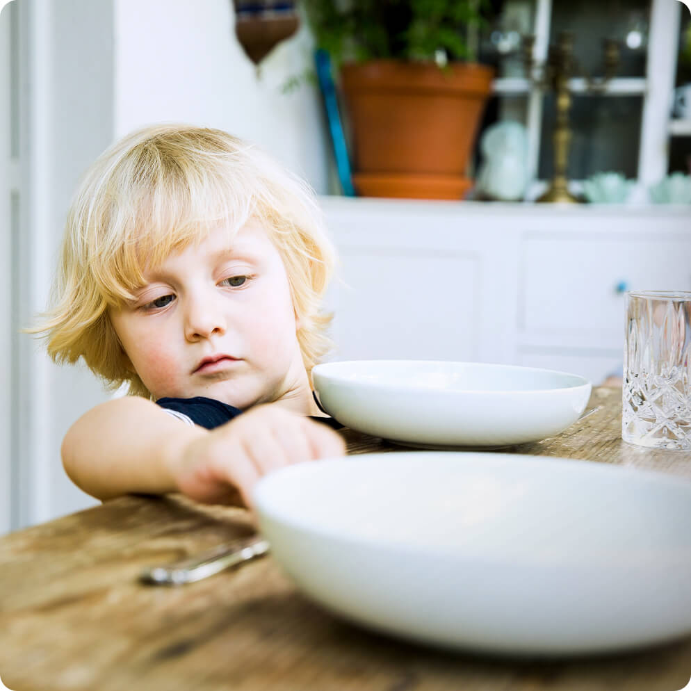 A young child setting the table with plates, silverware and glasses