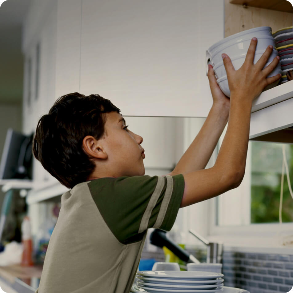 A young boy putting away a stack of bowls in the cabinet