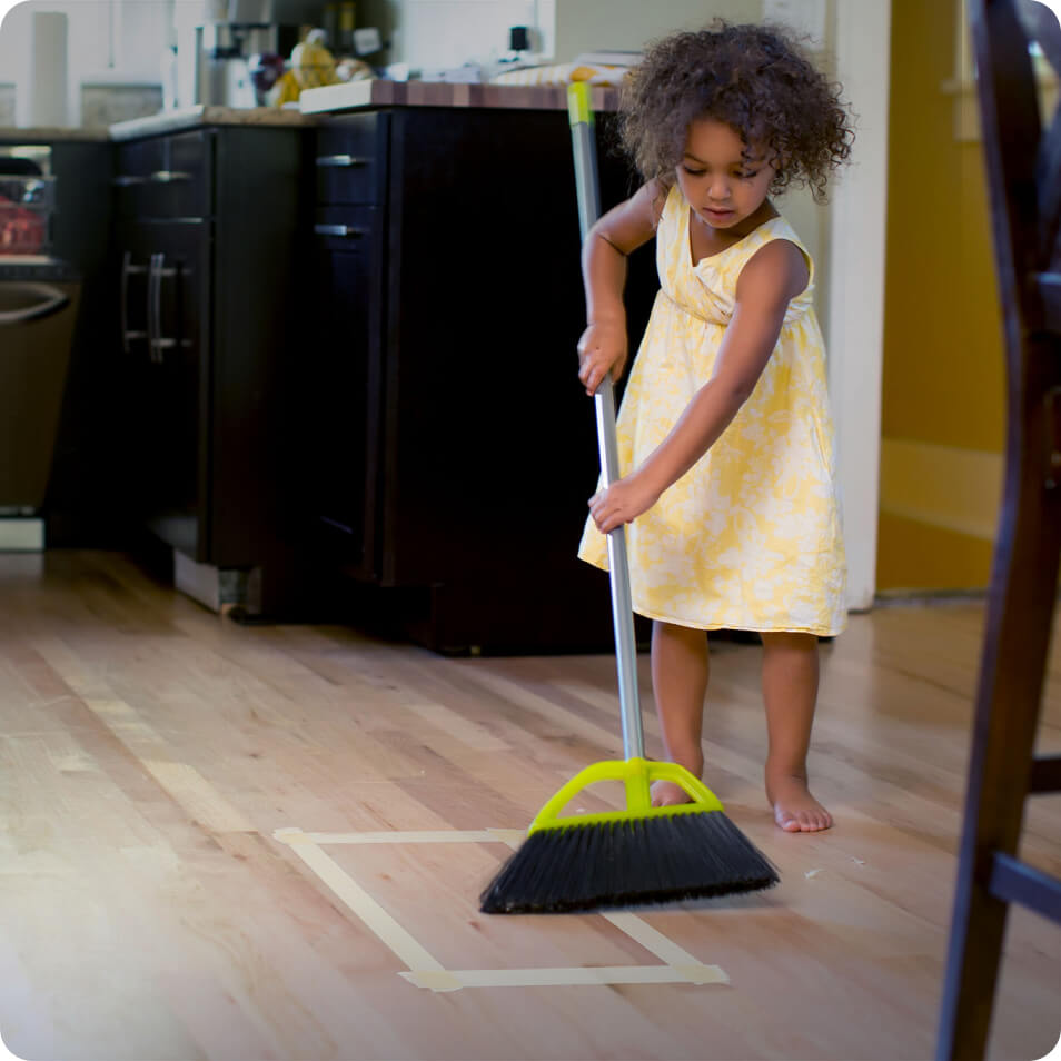 A girl sweeping crumbs into a taped square on the floor