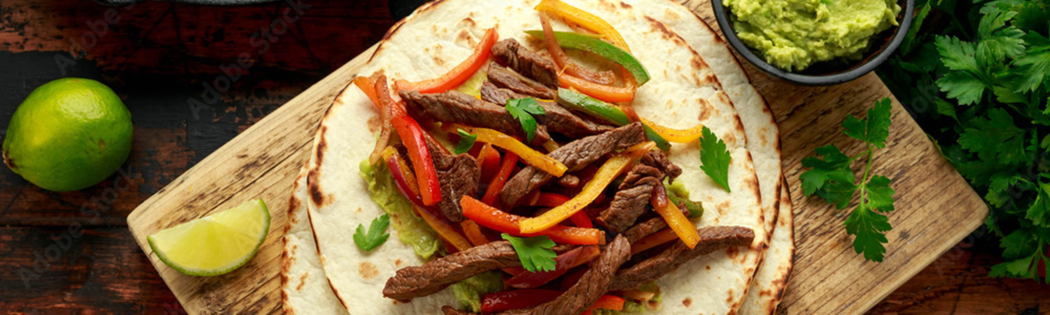 Flank steak fajita with bell peppers and tortilla on a wood serving board