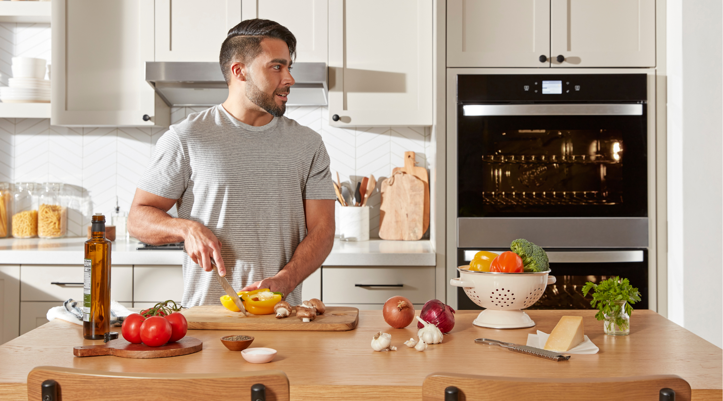 A person chopping vegetables at a kitchen island with a Whirlpool® Standard Double Wall Oven in the background