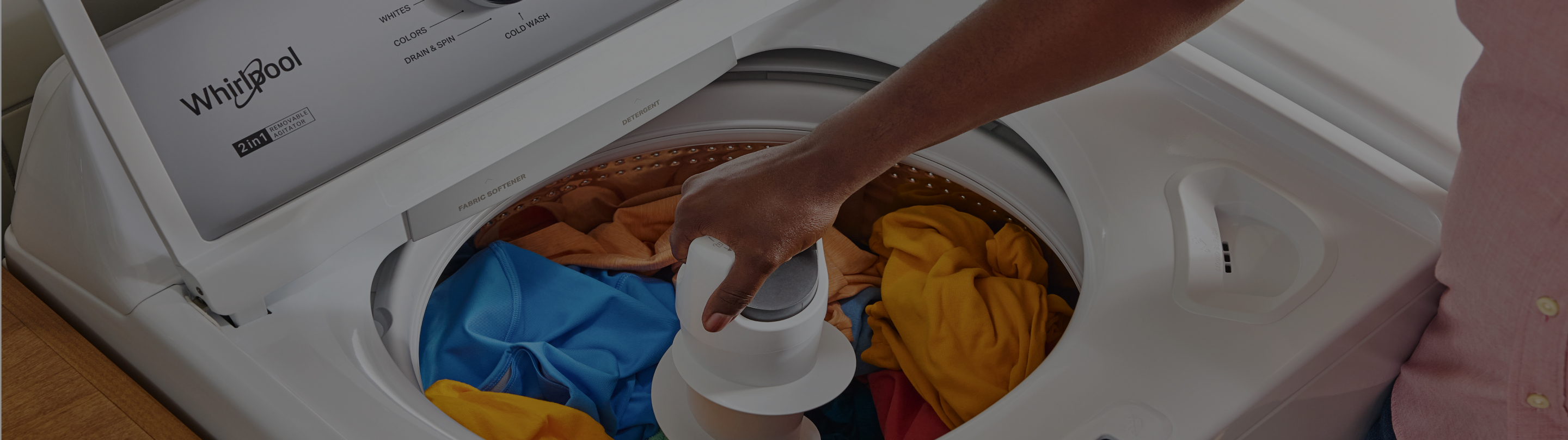 A person loads laundry in a Whirlpool® Top Load Washer and Dryer set