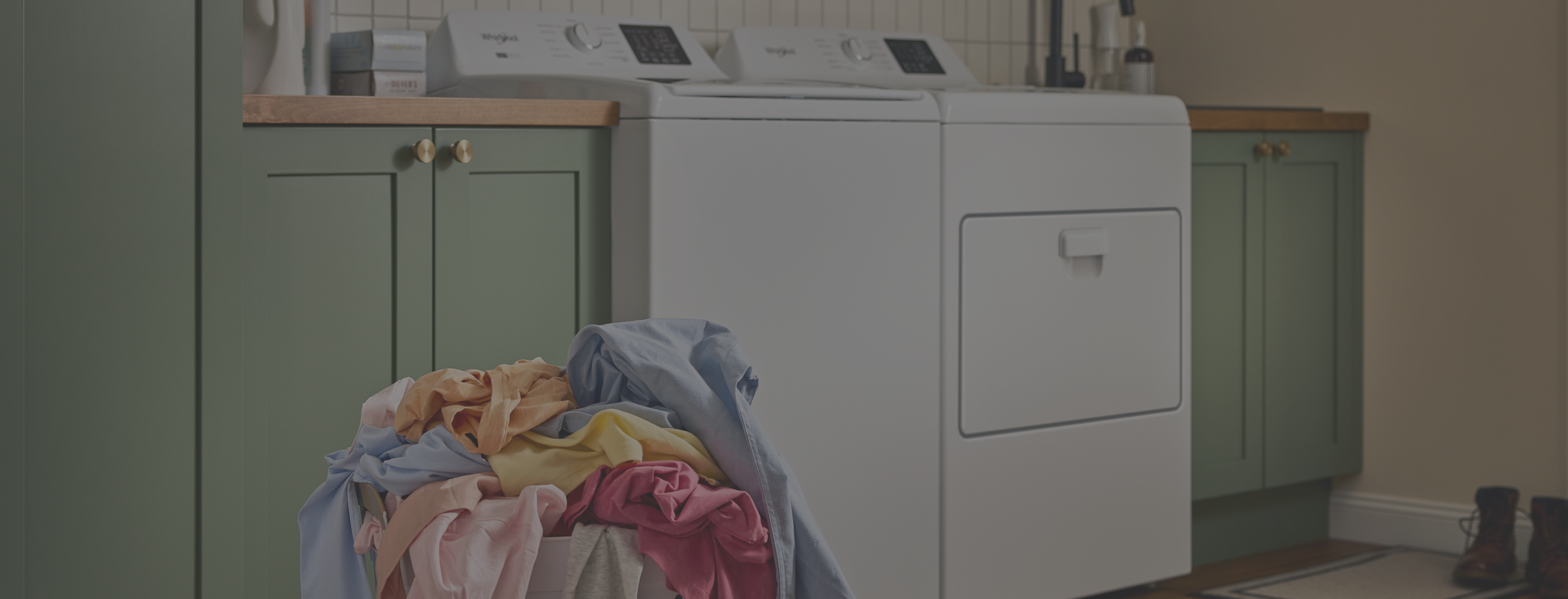A person loads laundry in a Whirlpool® Top Load Washer and Dryer set