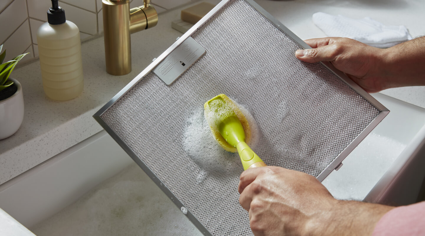 Person scrubbing a filter from a range hood