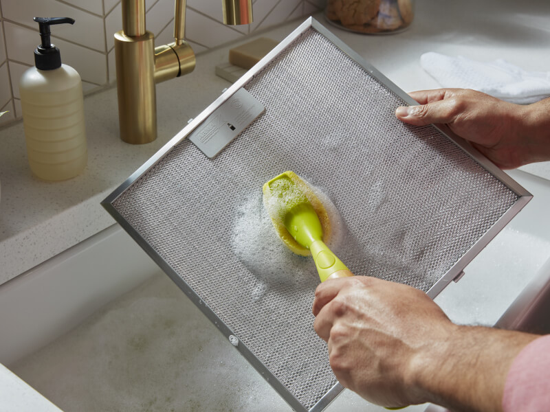 Person scrubbing a filter from a range hood Person scrubbing a filter from a range hood