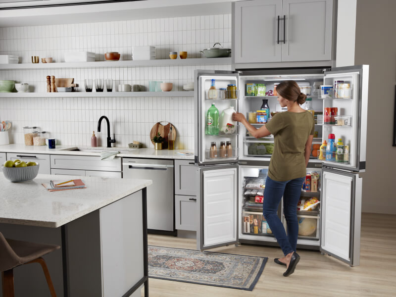 Person standing in front of an open fridge, removing items Person standing in front of an open fridge, removing items