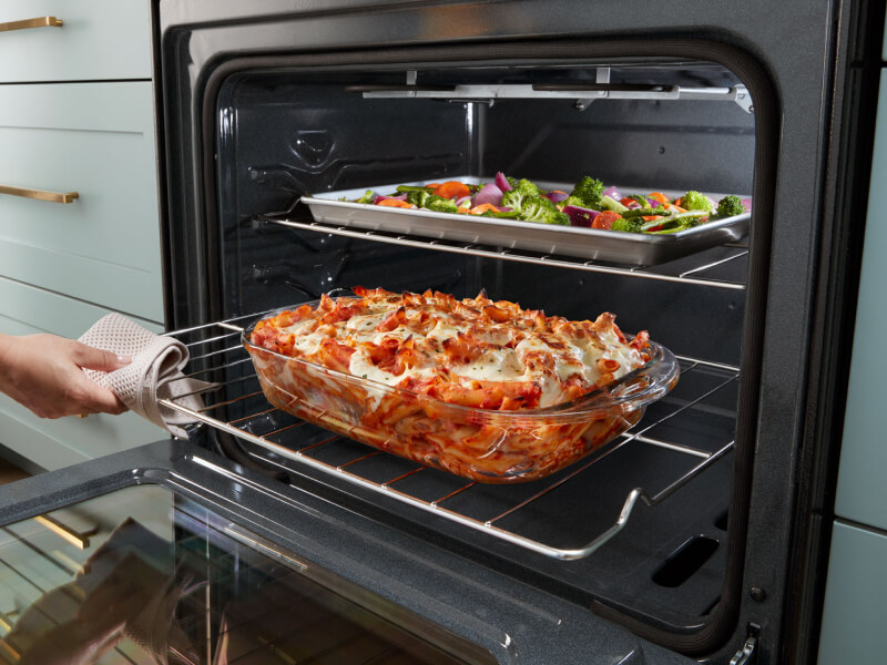 Person sliding out lower oven rack with lasagna on top Person sliding out lower oven rack with lasagna on top