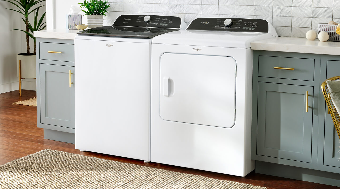 A white Whirlpool® Top Load Washer and Dryer in a laundery room with gray cabinetry