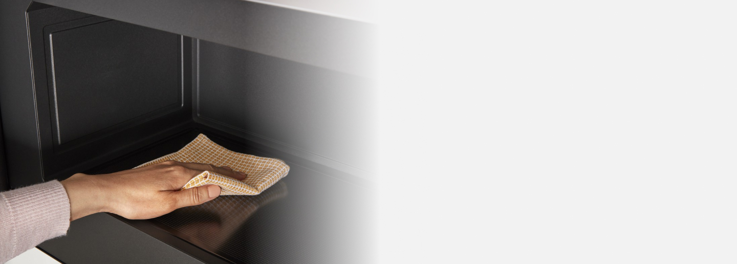 Person cleaning the interior of a microwave with a cloth