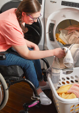 Person in a wheelchair loading laundry in a front load washer