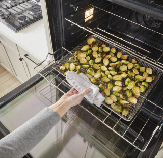 A person removing a tray of roasted vegetables from an oven