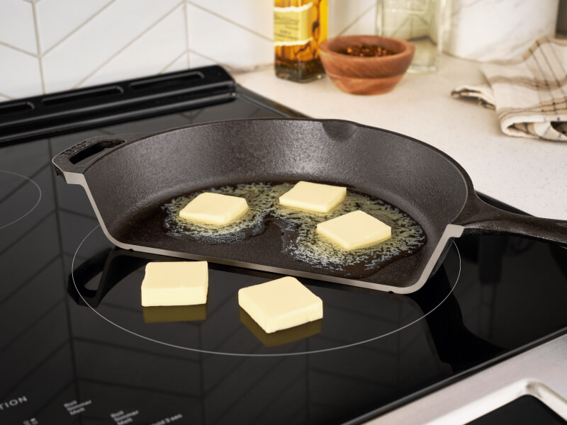 Photo of half a pan on a stove with butter melting on it, and next to it, non-melting pads of butter on the cooktop