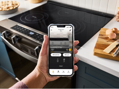 A hand holding a cell phone in the foreground with an induction cooktop in the background