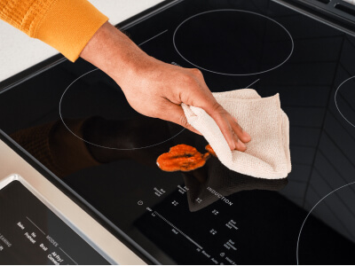 A hand cleaning up a spill on an induction cooktop