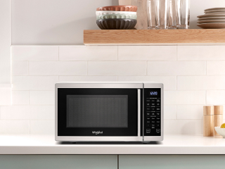 A countertop microwave underneath a brown shelf
