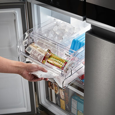 Person sliding ice drawer out of bottom-left 4-door compartment