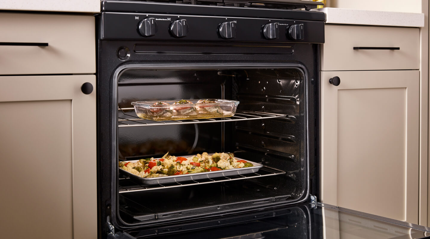 An oven with chicken and a medley of veggies baking inside