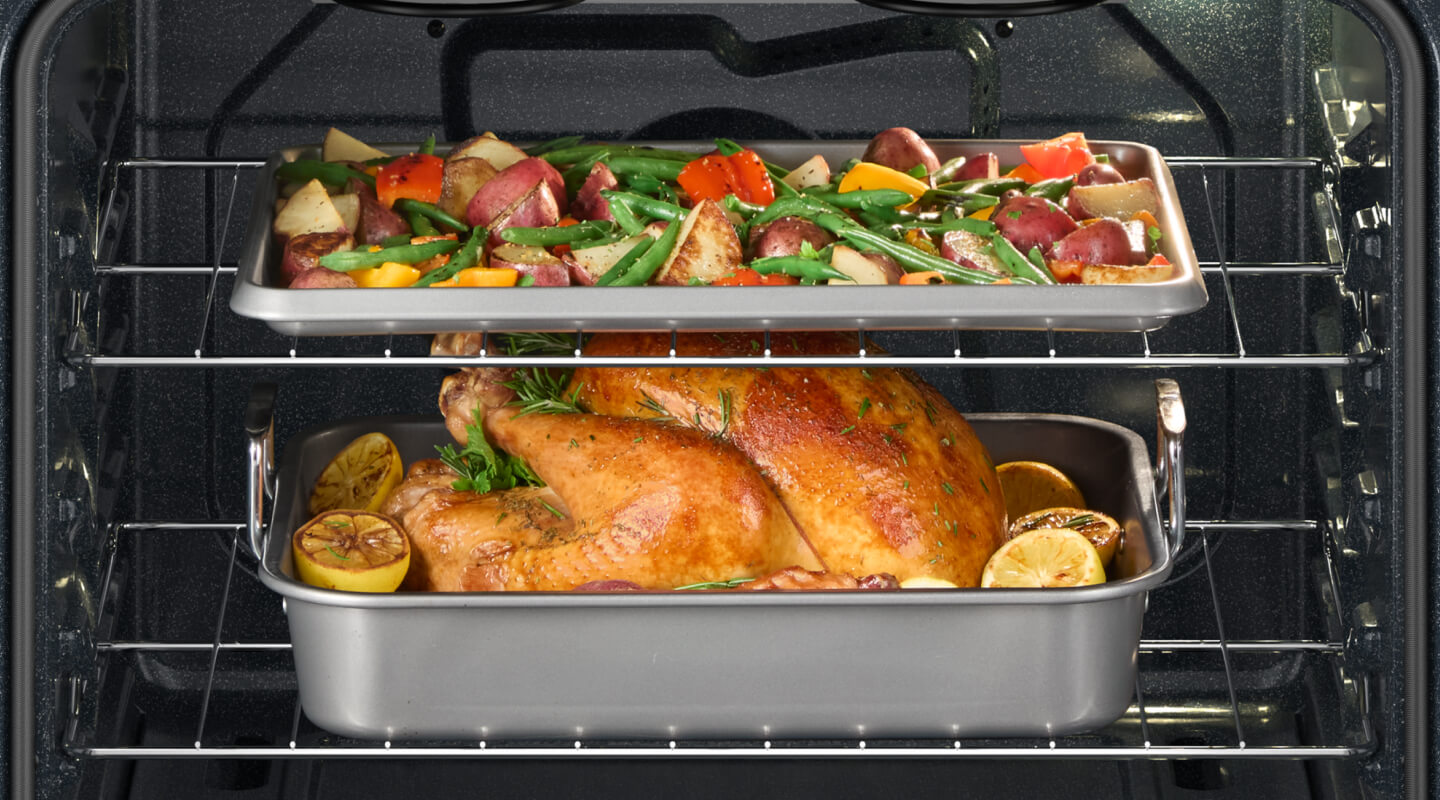 A chicken and vegetables on different racks in an oven