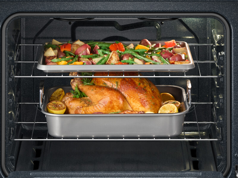 A chicken and vegetables on different racks in an oven