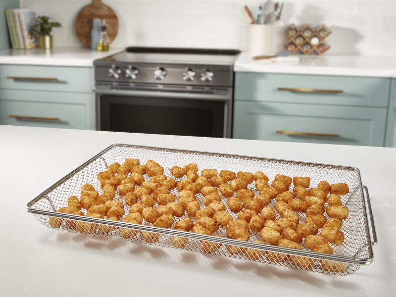 An air fry basket with tater tots sitting on a white countertop. An air fry basket with tater tots sitting on a white countertop.