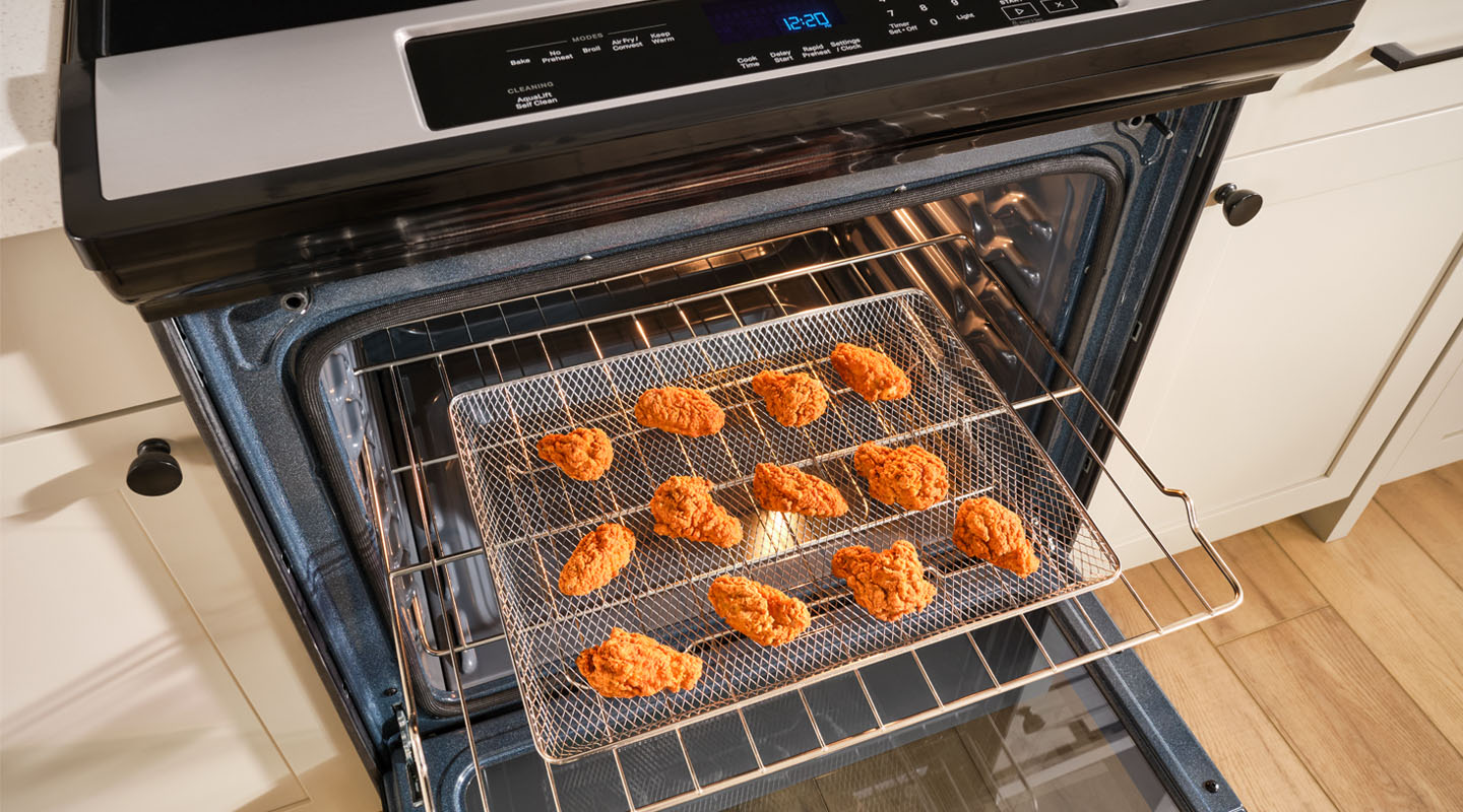 Open oven with chicken wings in a fryer basket