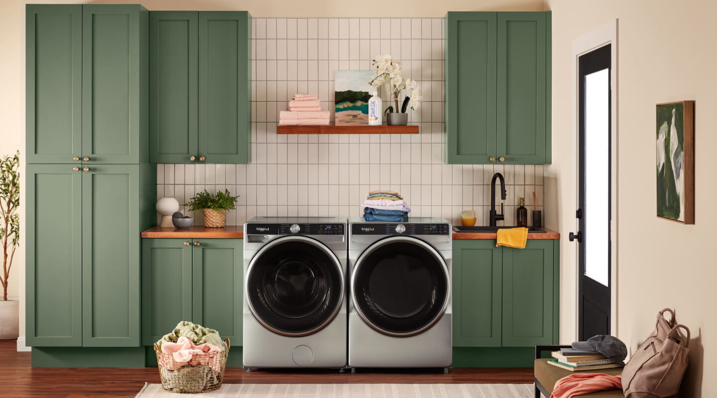 Whirlpool® washer and dryer set in a laundry room with green cabinetry and white tile