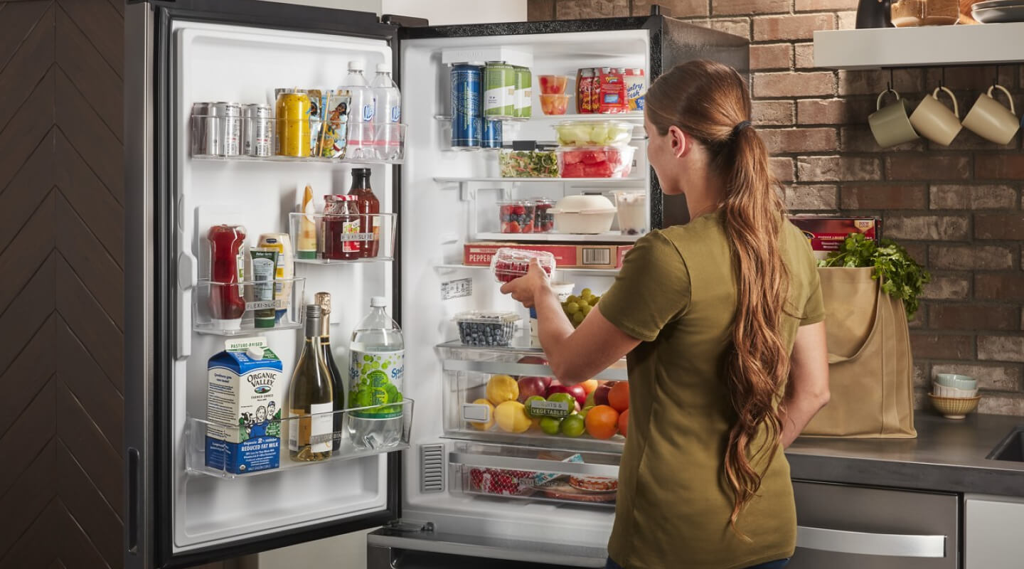  A woman standing in front of an open, bottom-freezer refrigerator