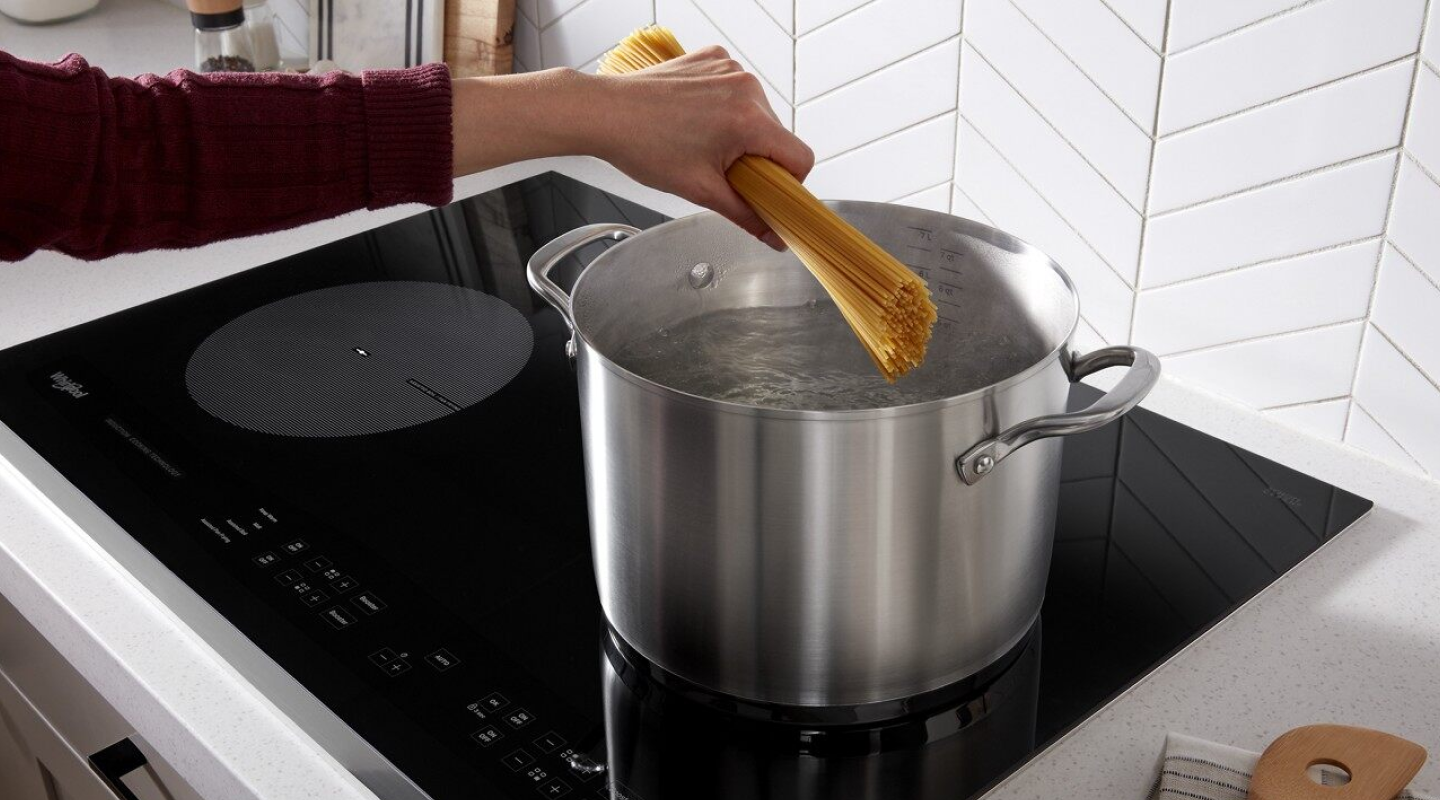 A person boiling spaghetti noodles on an electric cooktop.