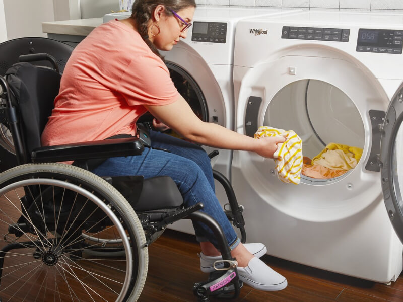 A person in a wheelchair putting clothes into a Whirlpool® Dryer