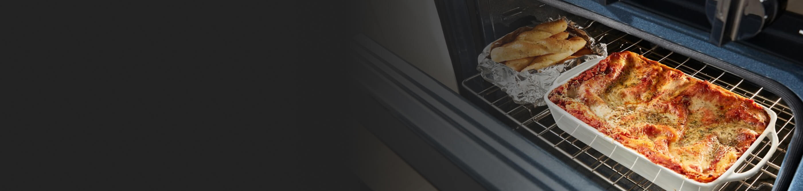 A lasagna and long rolls on a rack in the oven