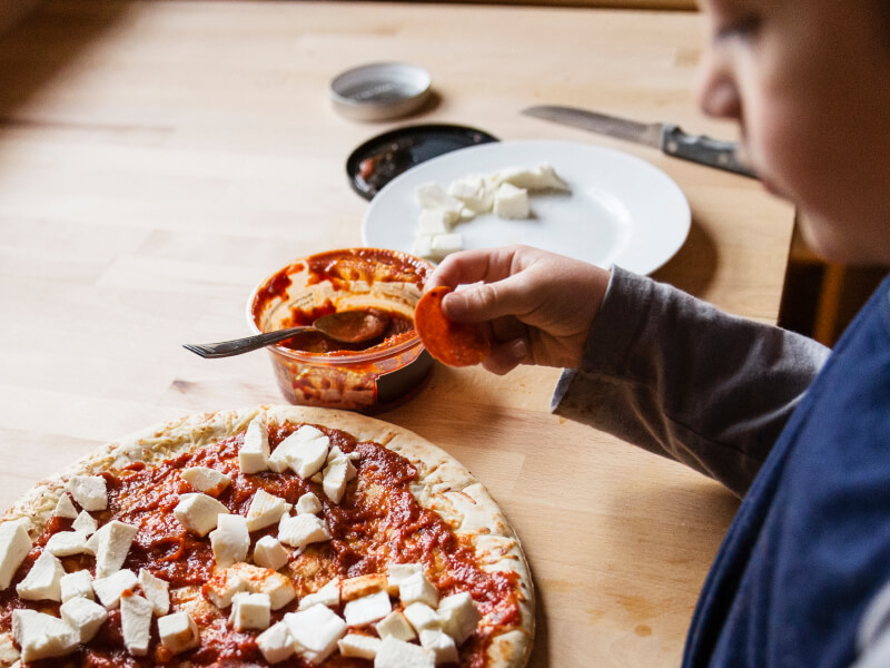 A kid placing toppings on a pizza A kid placing toppings on a pizza