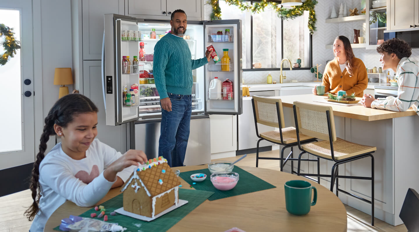 A group of people in a kitchen while a child builds a gingerbread house