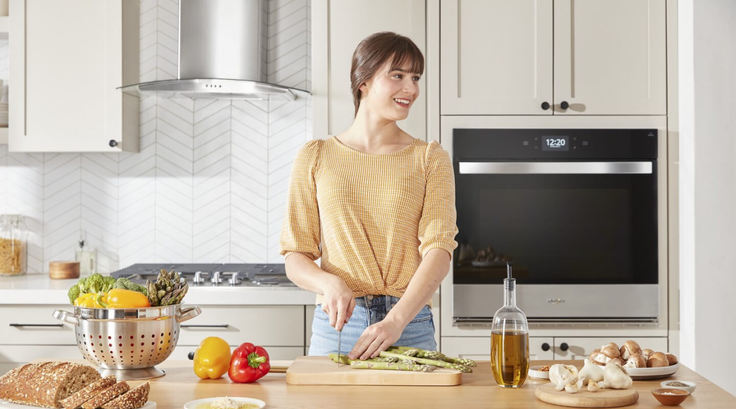 Person standing at a kitchen island chopping vegetables on a cutting board