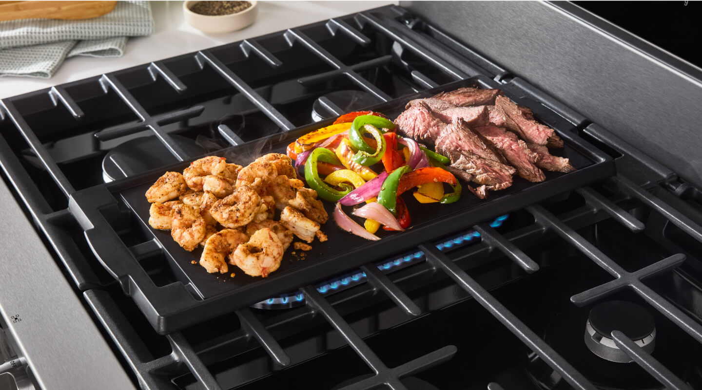 Meat and vegetables cooking on a stovetop griddle Meat and vegetables cooking on a stovetop griddle