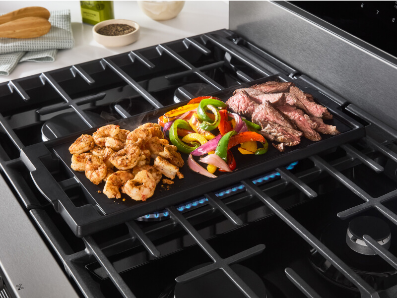 Meat and vegetables cooking on a stovetop griddle Meat and vegetables cooking on a stovetop griddle