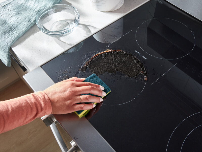 Person cleaning a spill on an electric cooktop Person cleaning a spill on an electric cooktop