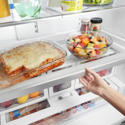 Person adjusting a shelf with lasagna and a bowl of berries on top