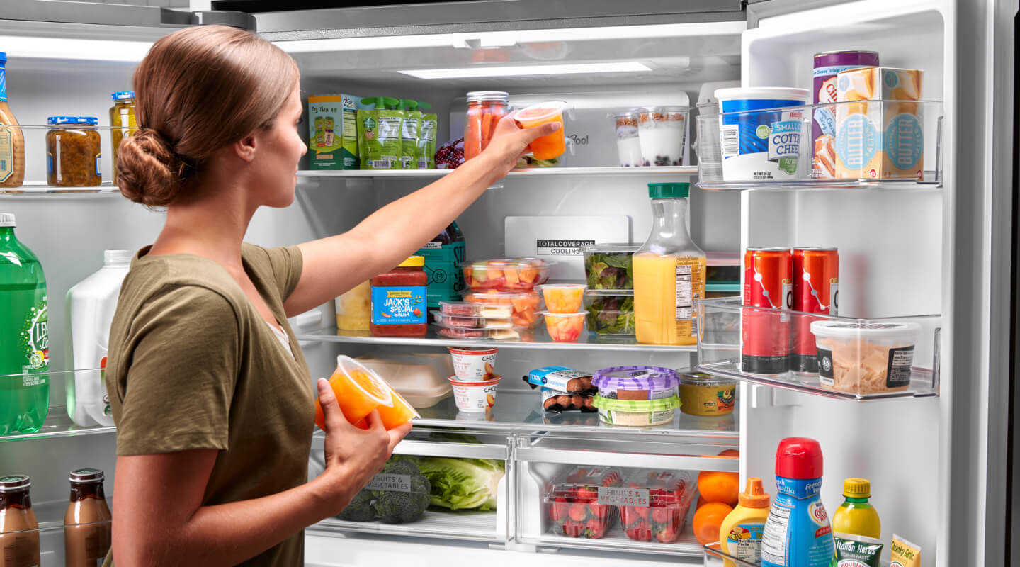 Woman opening a refrigerator door and selecting a container of fruit