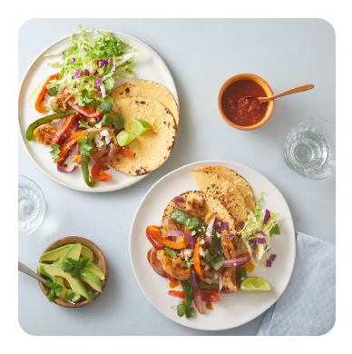 Two white dinner plates with fajitas and a side of avocado and salsa