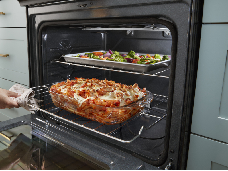 Person pulling out lasagna from the low oven rack while vegetables cook on the top rack Person pulling out lasagna from the low oven rack while vegetables cook on the top rack