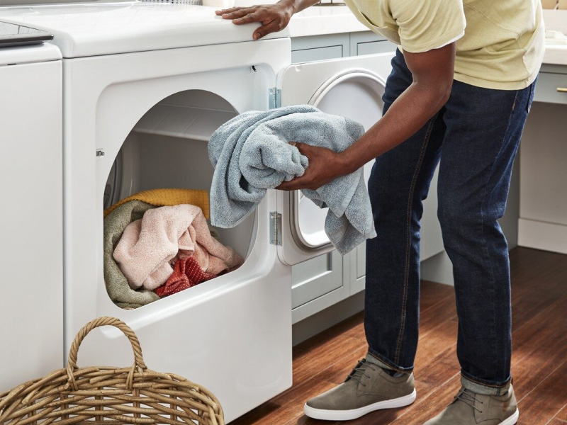 Person placing a load of towels into the dryer Person placing a load of towels into the dryer